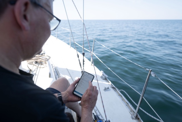 Segler sitzt an Deck und Bereitet die Sonde per App auf dem Telefon vor.