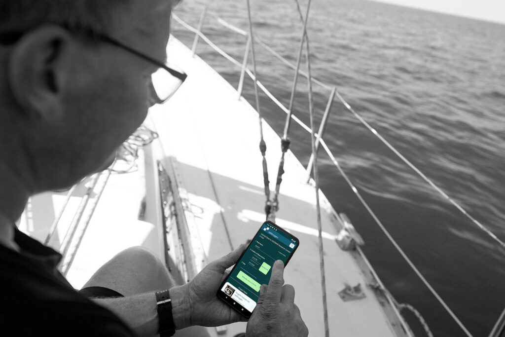 Mockup. Segler mit Handy und laufender app auf einem Segelboot.